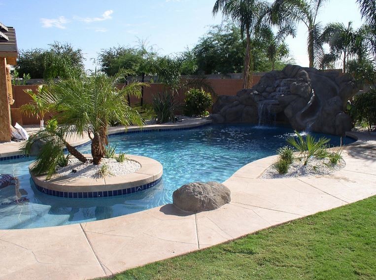 Imagen de piscina con tobogán natural tropical grande a medida en patio trasero con suelo de hormigón estampado