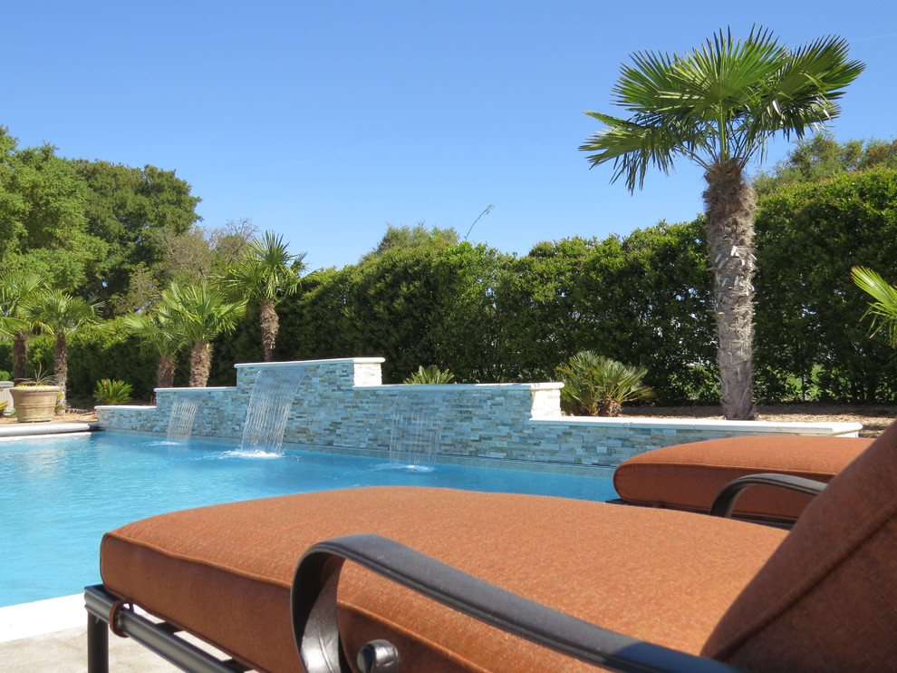 Modelo de piscina con fuente de estilo americano de tamaño medio rectangular en patio trasero con losas de hormigón