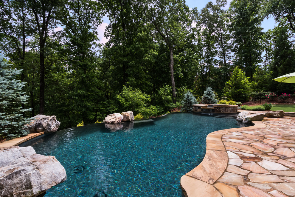Immagine di un'ampia piscina a sfioro infinito tradizionale personalizzata dietro casa con una vasca idromassaggio e pavimentazioni in pietra naturale