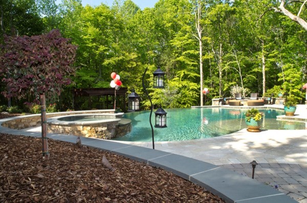 Aménagement d'une grande piscine à débordement et arrière classique sur mesure avec un bain bouillonnant et des pavés en pierre naturelle.