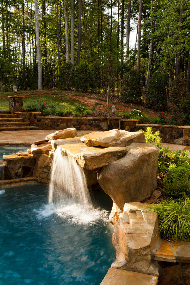 This is an example of a traditional natural swimming pool in Charlotte with a water feature.