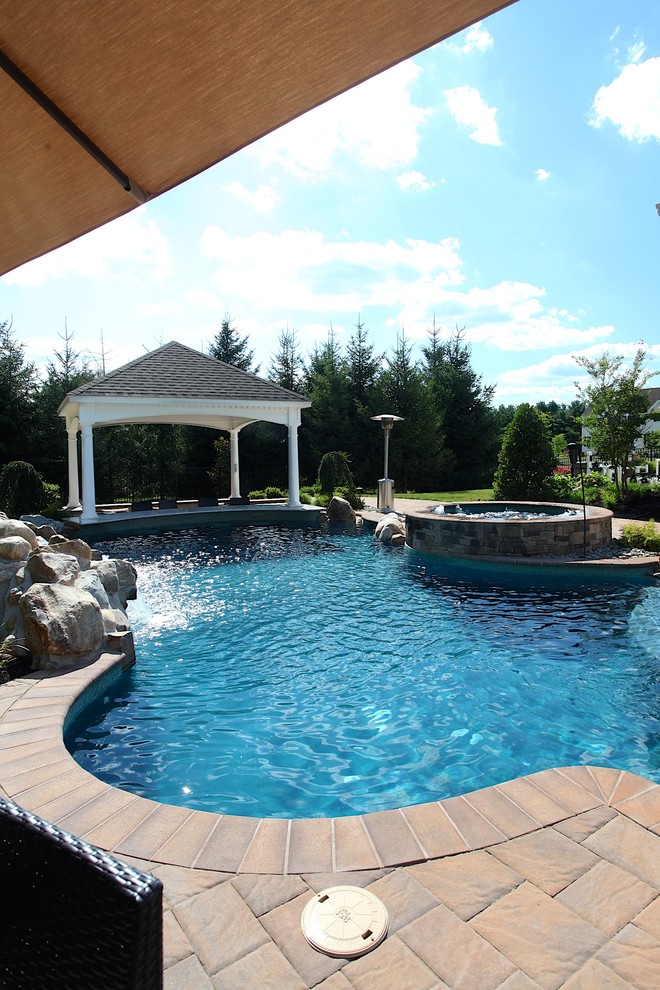 Diseño de piscinas y jacuzzis clásicos grandes a medida en patio trasero con adoquines de hormigón