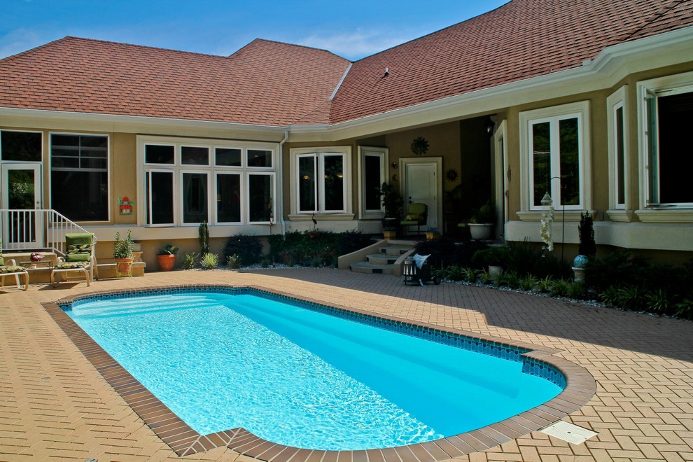 Foto de piscina alargada tradicional de tamaño medio a medida en patio trasero con adoquines de hormigón