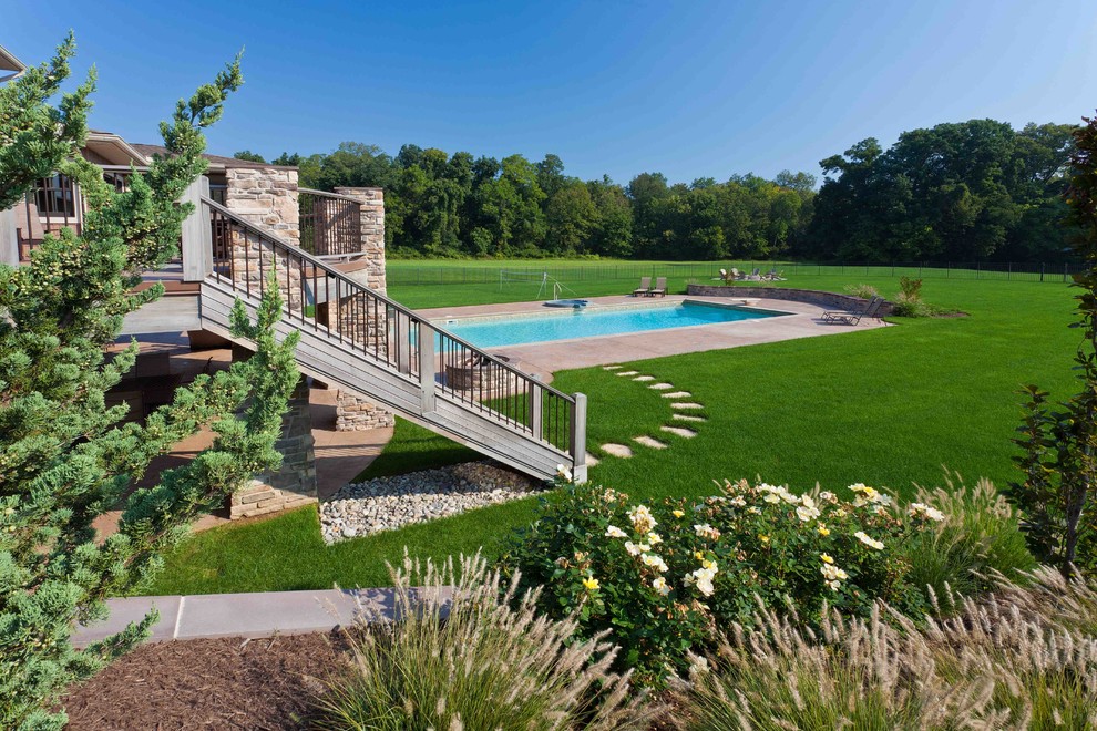 Diseño de piscina alargada de estilo de casa de campo grande rectangular en patio trasero con adoquines de hormigón