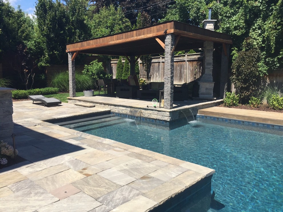 Ejemplo de piscina con fuente alargada clásica renovada grande en forma de L en patio trasero con adoquines de piedra natural