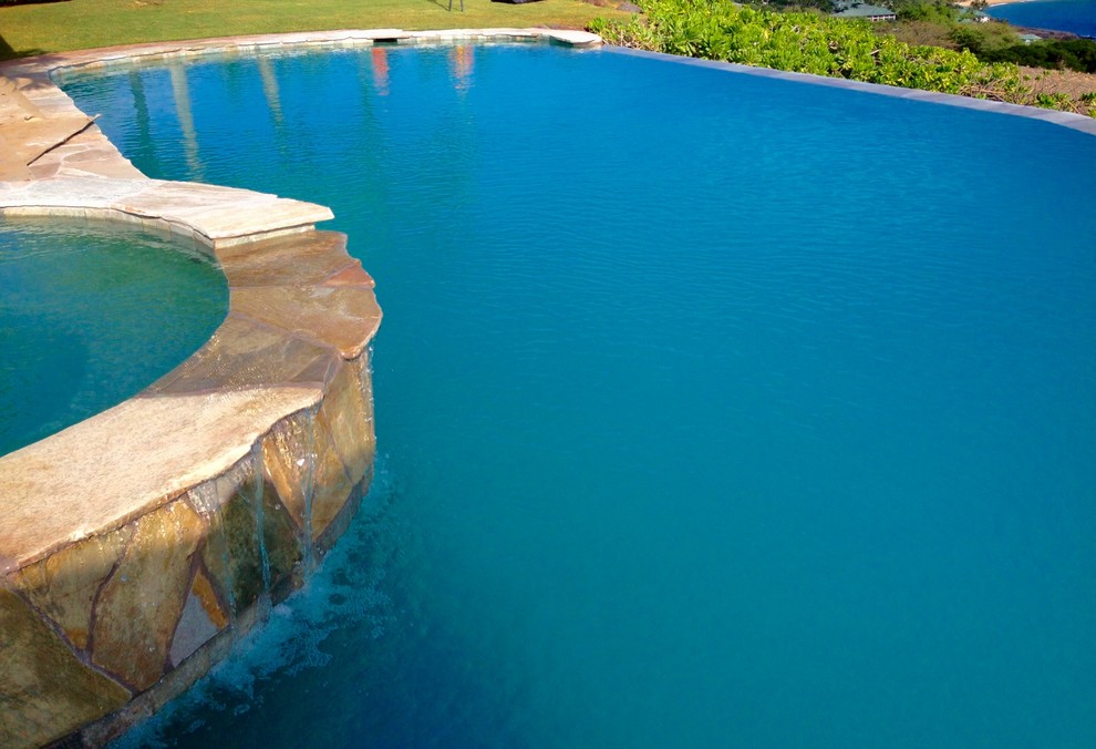 Diseño de piscinas y jacuzzis infinitos costeros grandes redondeados en patio trasero con adoquines de piedra natural