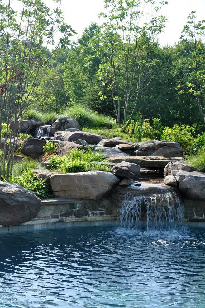 На фото: огромный естественный бассейн произвольной формы на заднем дворе в стиле фьюжн с водной горкой и покрытием из каменной брусчатки с