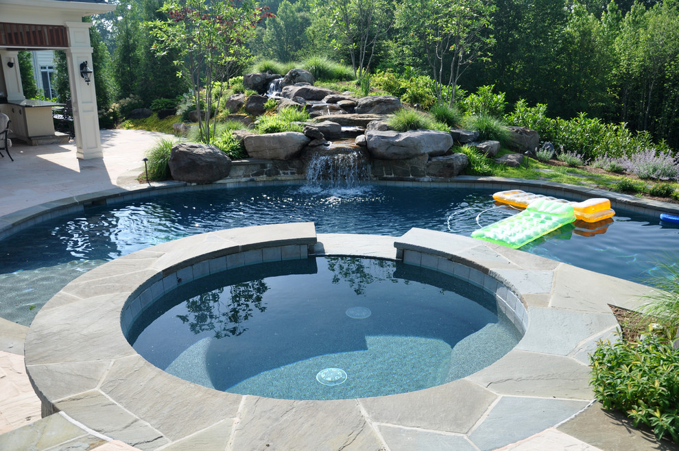 Cette image montre une très grande piscine naturelle et arrière bohème sur mesure avec un toboggan et des pavés en pierre naturelle.
