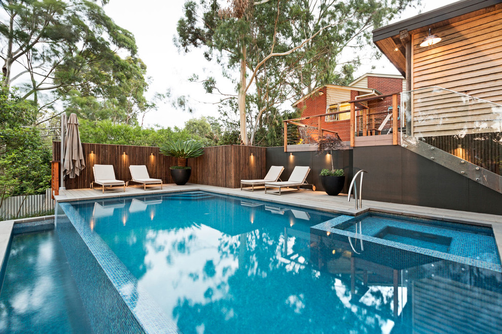 Modelo de casa de la piscina y piscina infinita contemporánea de tamaño medio rectangular en patio trasero con suelo de baldosas