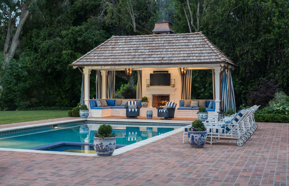 Ejemplo de casa de la piscina y piscina alargada tradicional grande rectangular en patio trasero con adoquines de ladrillo