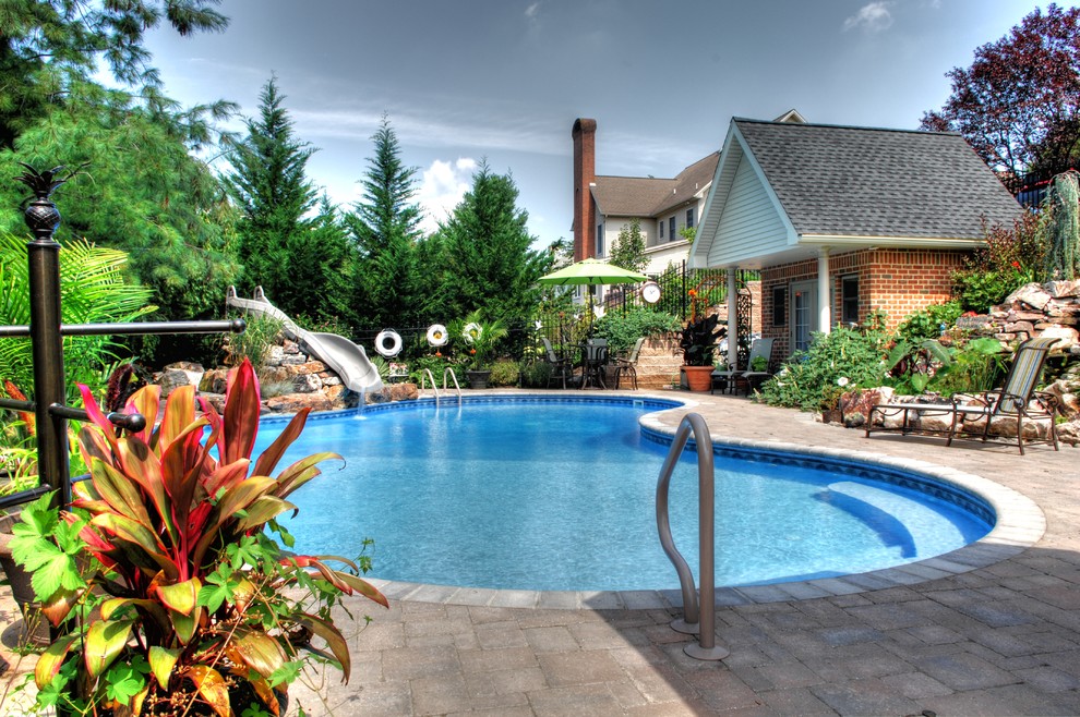 Foto de piscina con tobogán alargada tropical grande a medida en patio trasero con adoquines de hormigón