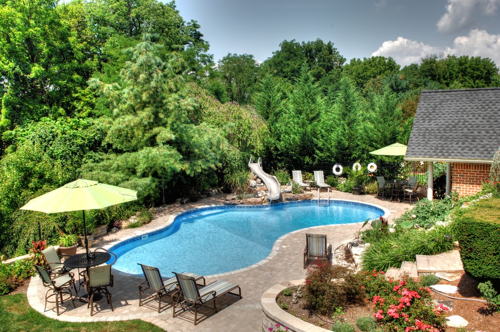 Foto de piscina con tobogán alargada exótica grande a medida en patio trasero con adoquines de hormigón