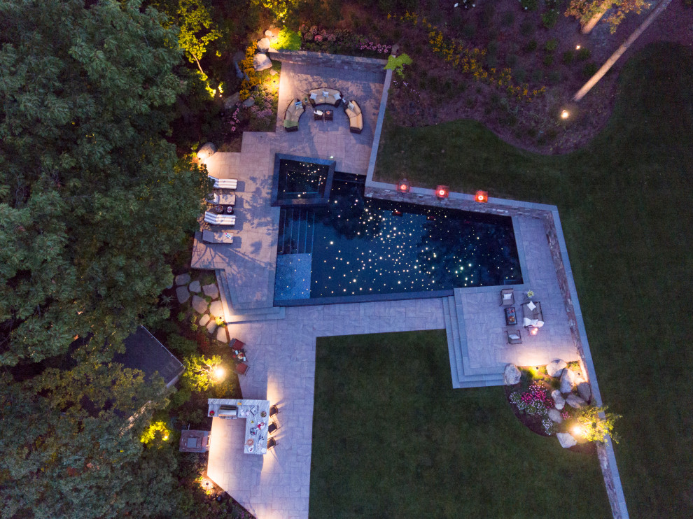 Foto de piscina elevada contemporánea grande en forma de L en patio trasero con suelo de baldosas