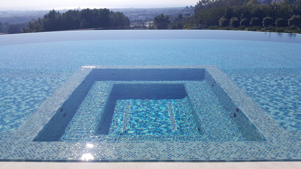 Esempio di una grande piscina a sfioro infinito design rettangolare dietro casa con una vasca idromassaggio e piastrelle