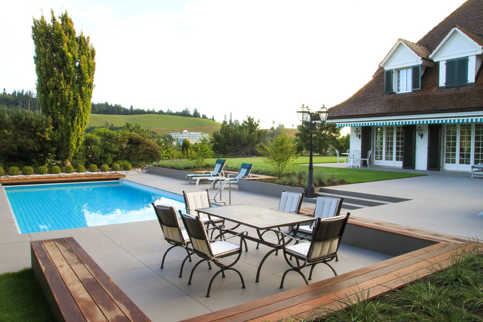 Modelo de piscina tradicional extra grande rectangular en patio con suelo de baldosas