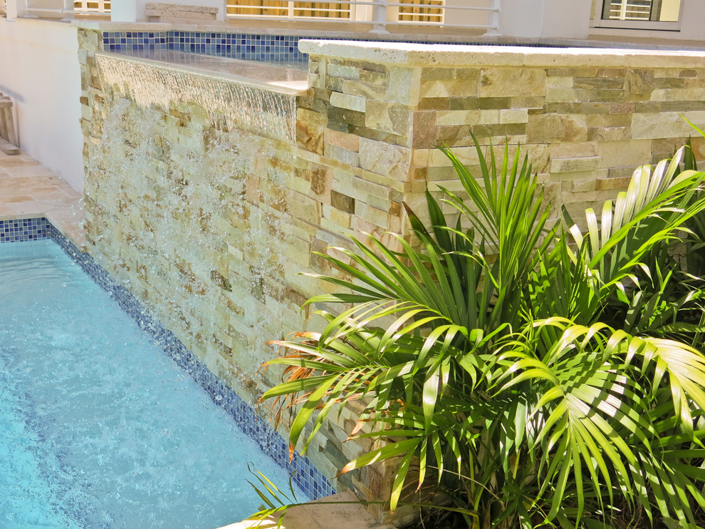 Ejemplo de piscina con fuente natural actual pequeña rectangular en patio trasero con adoquines de piedra natural