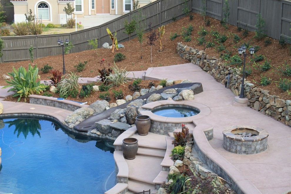 Imagen de piscina con tobogán clásica renovada grande a medida en patio trasero con adoquines de hormigón