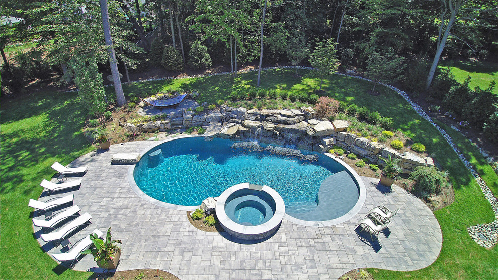 На фото: большой спортивный бассейн в форме фасоли на заднем дворе в морском стиле с джакузи и покрытием из каменной брусчатки с