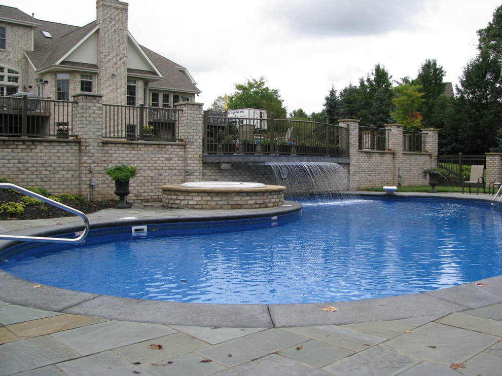 Aménagement d'une grande piscine arrière classique sur mesure avec un bain bouillonnant et des pavés en pierre naturelle.