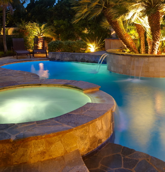 Foto på en stor tropisk pool på baksidan av huset, med en fontän och naturstensplattor