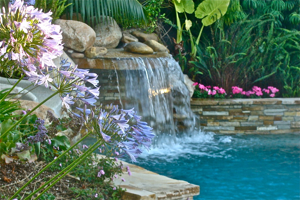 Exempel på en mellanstor exotisk anpassad pool på baksidan av huset, med en fontän och naturstensplattor