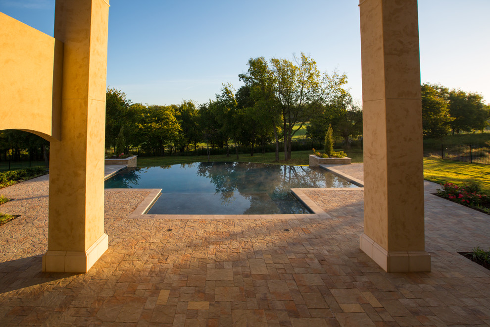 Ejemplo de piscina alargada tradicional grande a medida en patio trasero con adoquines de hormigón