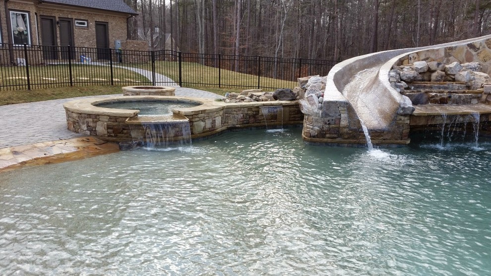 Cette photo montre une grande piscine naturelle et arrière montagne sur mesure avec un toboggan et des pavés en pierre naturelle.