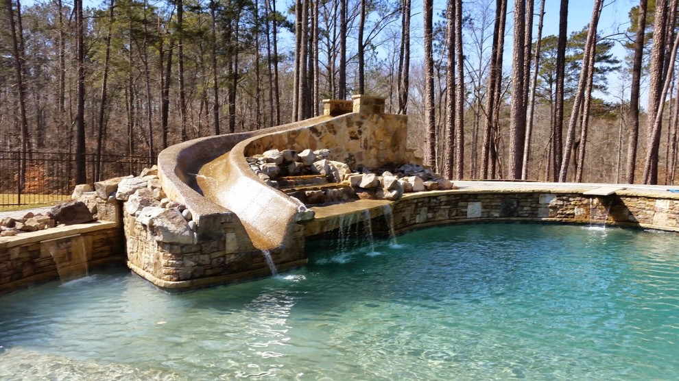 Cette image montre une grande piscine naturelle et arrière chalet sur mesure avec un toboggan et des pavés en pierre naturelle.