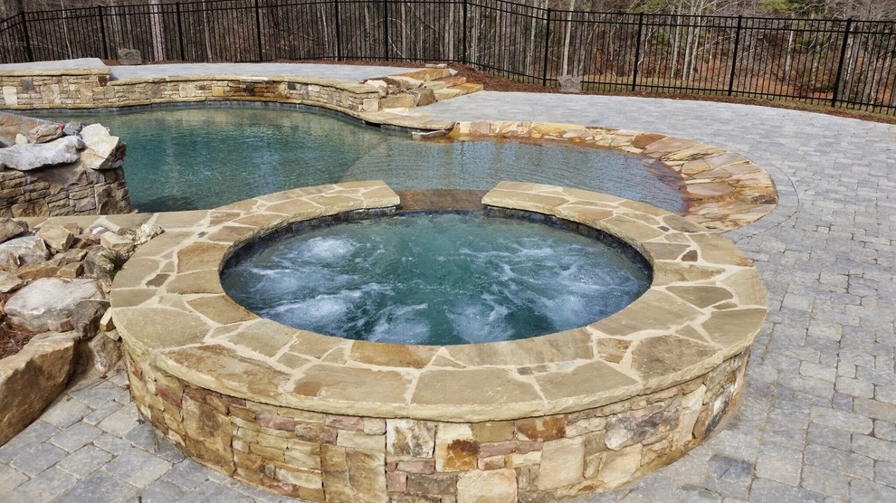 На фото: большой естественный бассейн произвольной формы на заднем дворе в стиле рустика с покрытием из каменной брусчатки и джакузи с