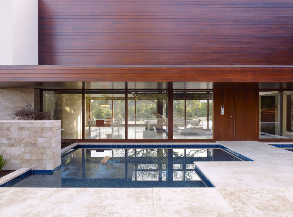 Diseño de piscina moderna grande en forma de L en patio trasero con adoquines de piedra natural