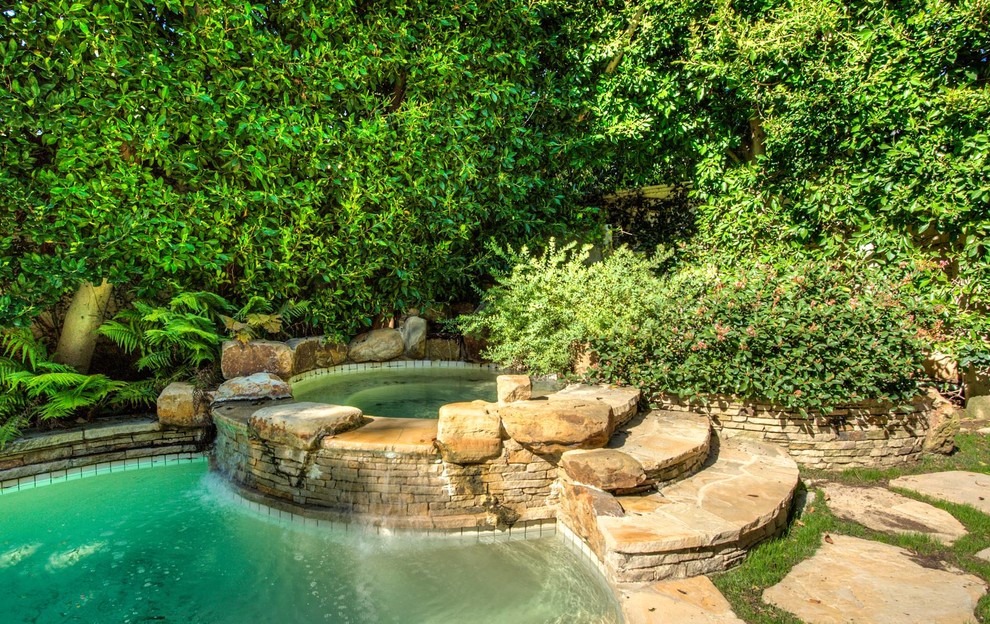 Стильный дизайн: большой естественный бассейн в форме фасоли на заднем дворе в стиле неоклассика (современная классика) с джакузи и покрытием из каменной брусчатки - последний тренд