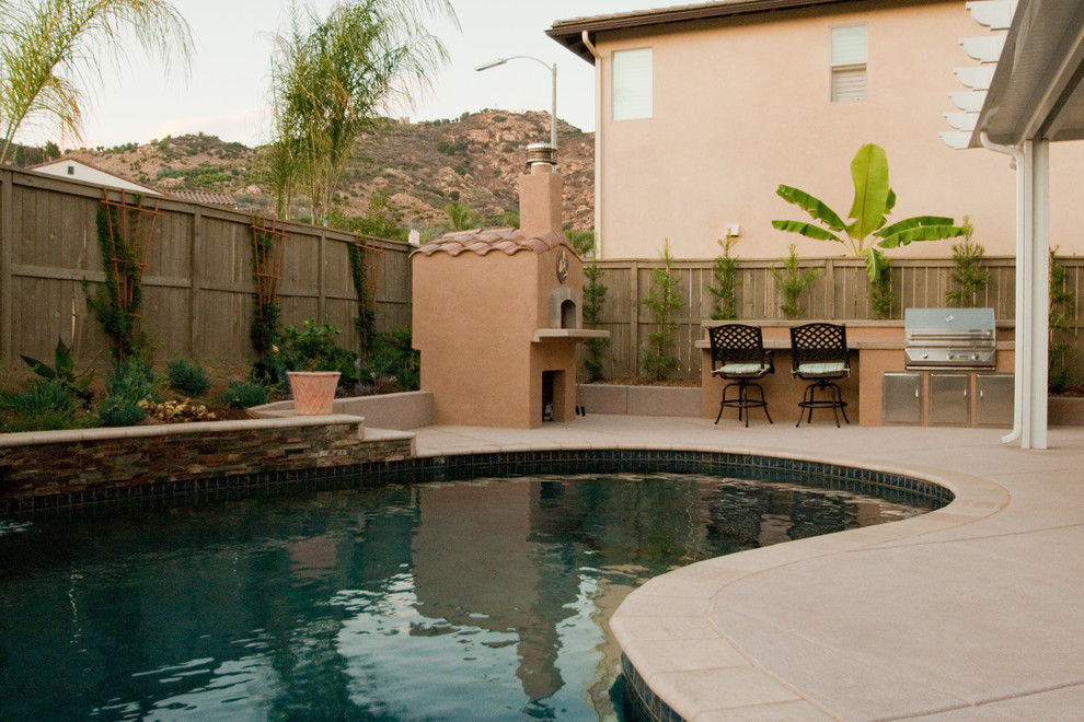 Esempio di una piscina naturale chic a "C" di medie dimensioni e dietro casa con fontane e pavimentazioni in cemento