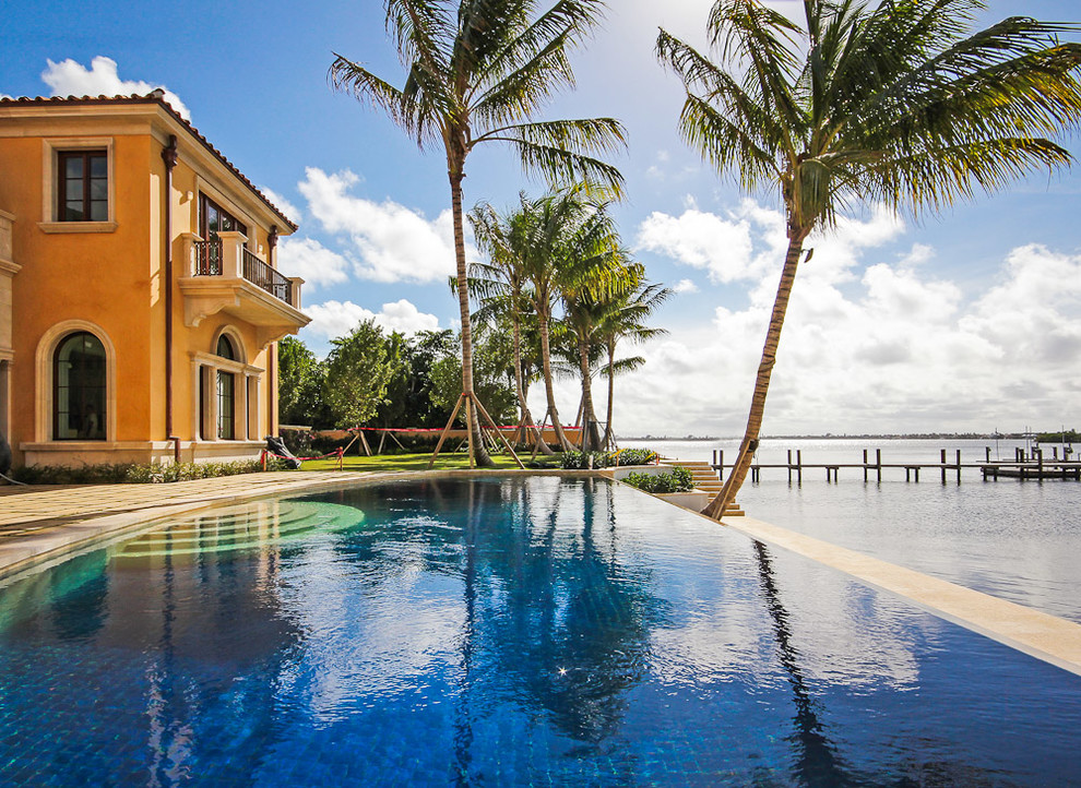 Immagine di una grande piscina a sfioro infinito mediterranea personalizzata dietro casa con pavimentazioni in pietra naturale