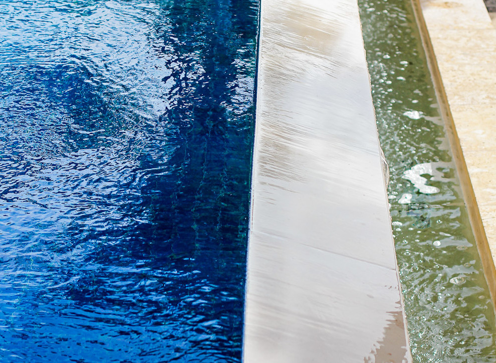 Modelo de piscina infinita mediterránea grande a medida en patio trasero con adoquines de piedra natural