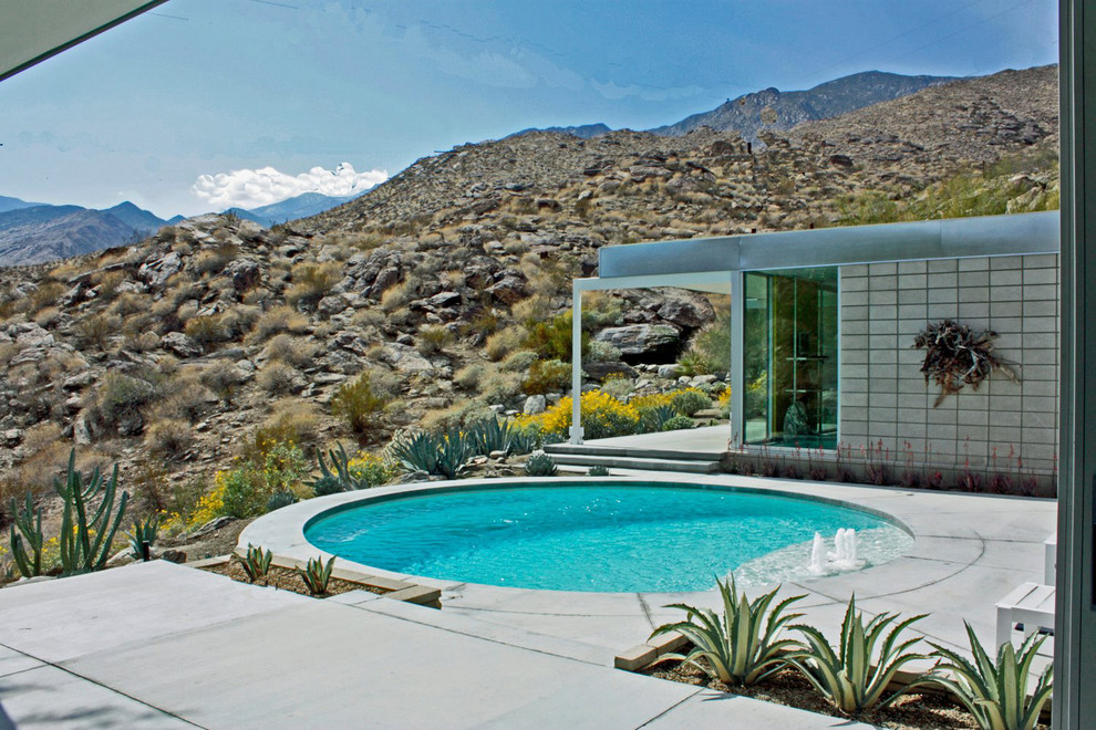 Immagine di una piscina moderna rotonda di medie dimensioni e dietro casa con lastre di cemento