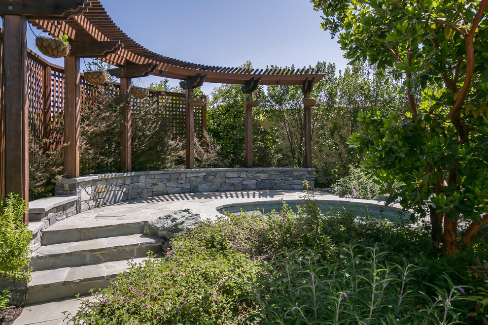 Inspiration för en liten tropisk rund baddamm på baksidan av huset, med en fontän och naturstensplattor
