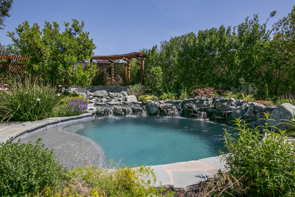 Immagine di una piccola piscina naturale tropicale rotonda dietro casa con fontane e pavimentazioni in pietra naturale
