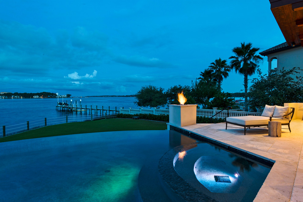This is an example of a large mediterranean back infinity swimming pool in Miami with a water feature and brick paving.