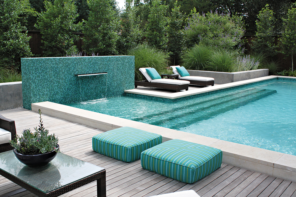 Cette photo montre une grande piscine arrière tendance sur mesure avec une terrasse en bois et un point d'eau.