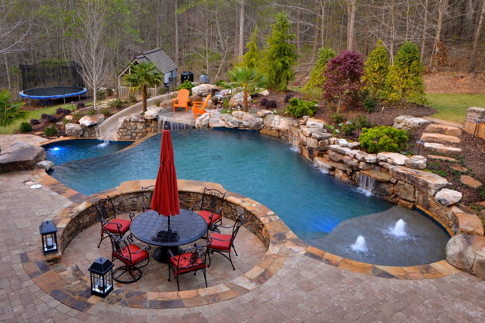 Ejemplo de piscina infinita rústica extra grande a medida en patio trasero con adoquines de piedra natural