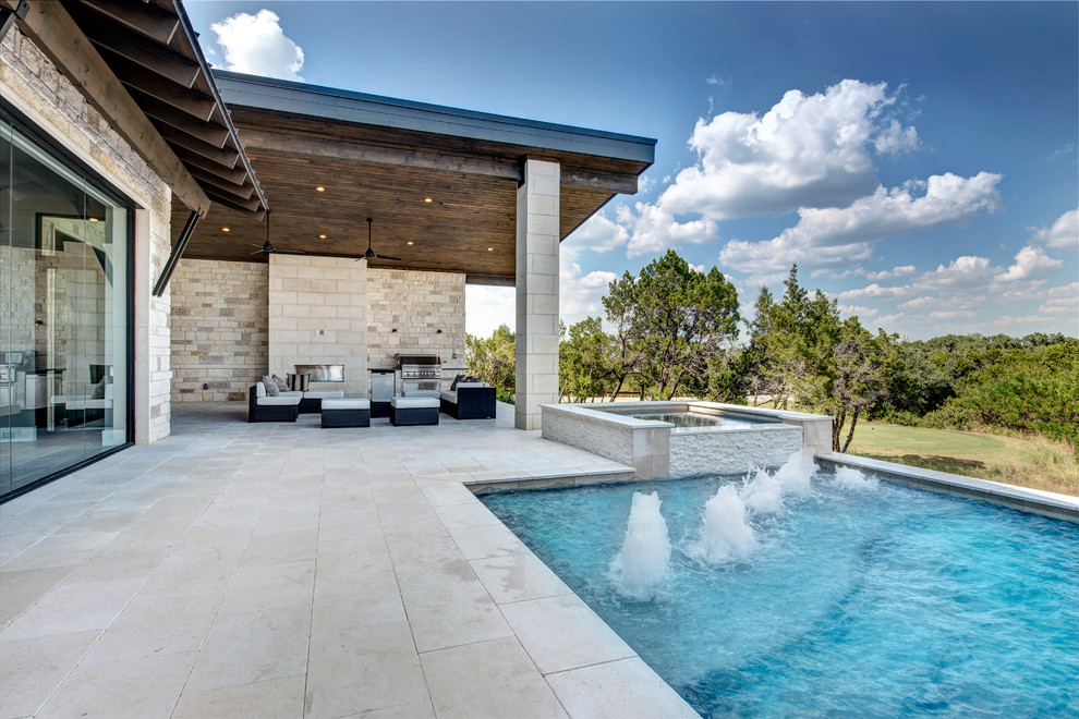 Large modern back rectangular infinity swimming pool in Austin with a water feature and natural stone paving.