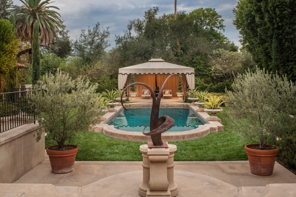 На фото: большой бассейн произвольной формы на заднем дворе в средиземноморском стиле с покрытием из бетонных плит