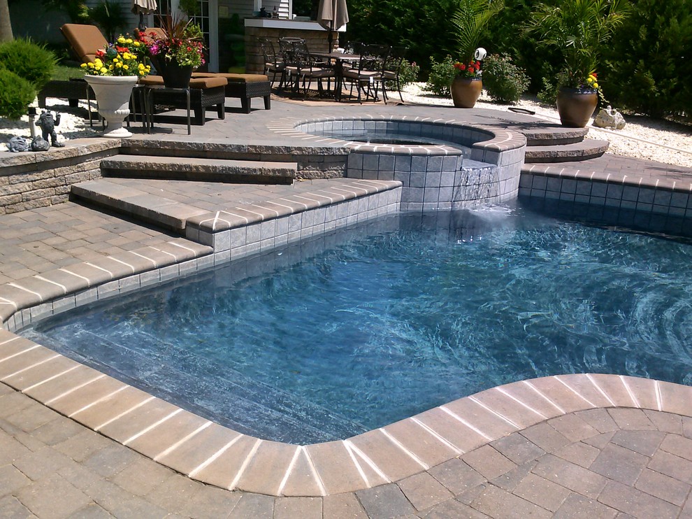 This is an example of a classic back custom shaped lengths hot tub in Orange County with brick paving.