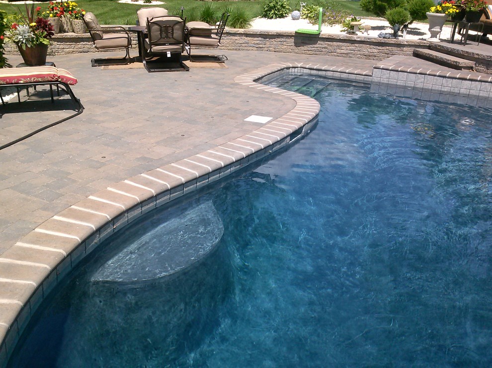 Photo of a classic back custom shaped lengths hot tub in Orange County with brick paving.