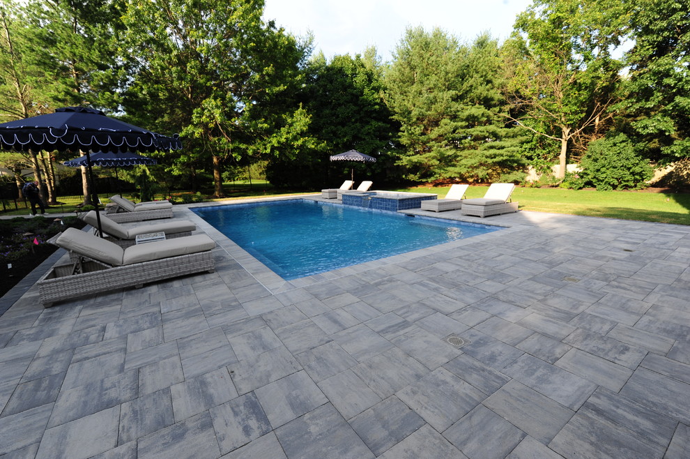 Modelo de piscinas y jacuzzis alargados tradicionales grandes rectangulares en patio trasero con adoquines de piedra natural