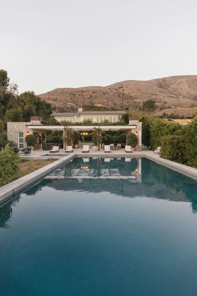 Ispirazione per un'ampia piscina a sfioro infinito stile marinaro rettangolare dietro casa con una dépendance a bordo piscina e pavimentazioni in cemento