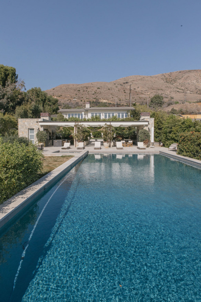 Modelo de casa de la piscina y piscina infinita costera extra grande rectangular en patio trasero con adoquines de hormigón