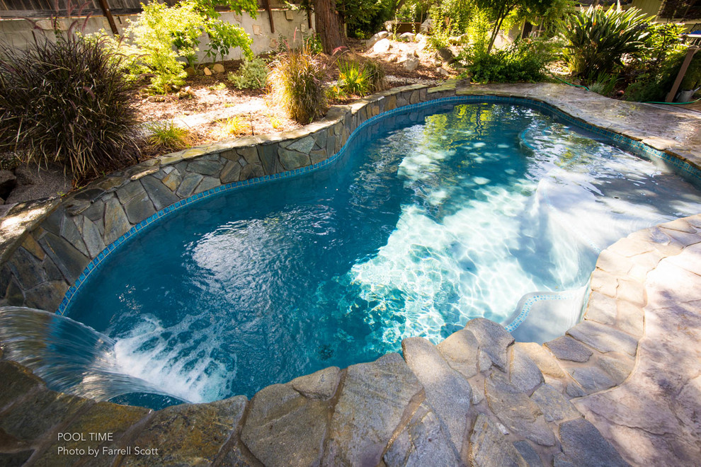 This is an example of a medium sized contemporary back custom shaped swimming pool in Sacramento with a water feature and stamped concrete.