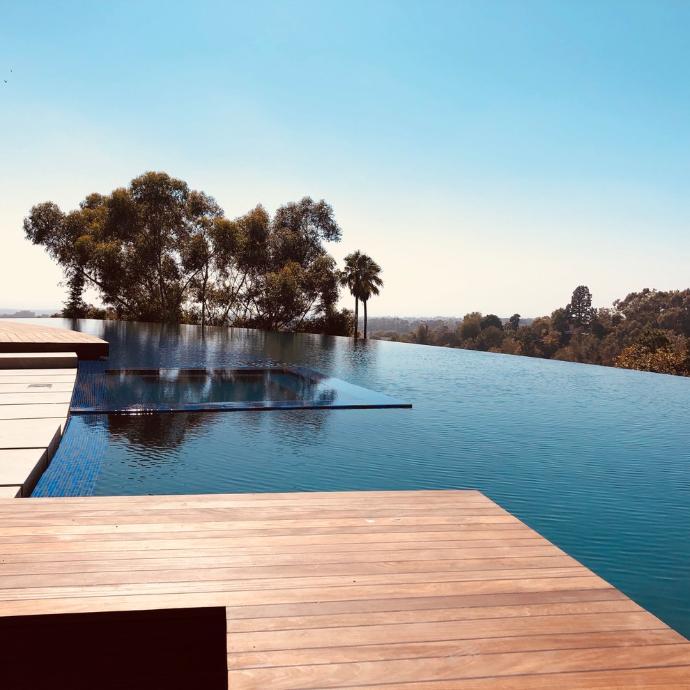 This is an example of a contemporary custom shaped infinity swimming pool in Los Angeles with decking.