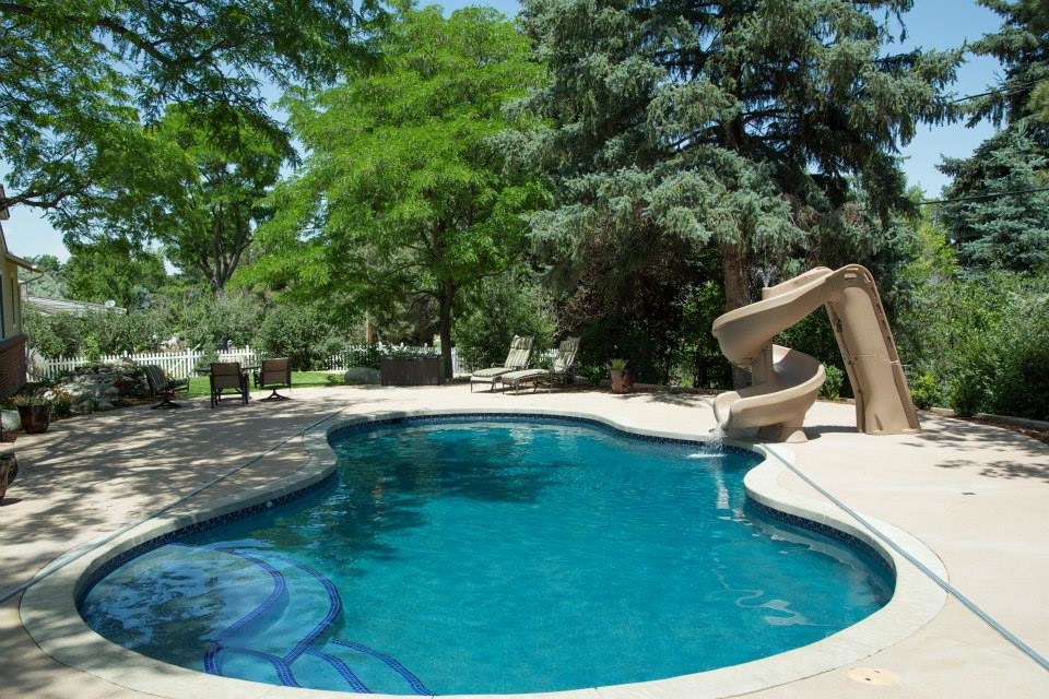 Exempel på en mellanstor klassisk anpassad pool på baksidan av huset, med vattenrutschkana och marksten i betong